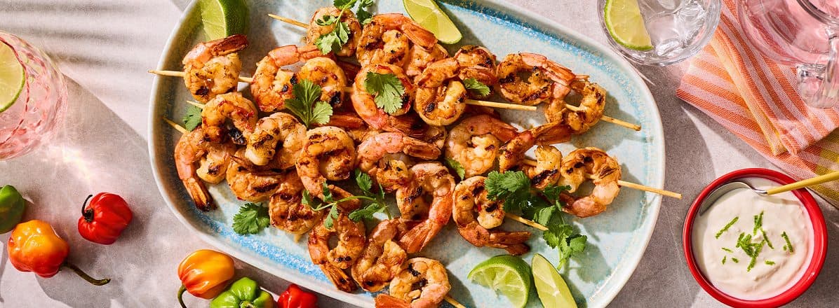 pale white and blue platter of Spicy BBQ Shrimp Skewers with Coconut Lime Yogurt on the side