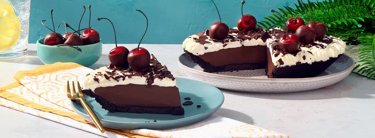 Chocolate cream pie topped with fresh chocolate dipped cherries with one slice taken out of it.
