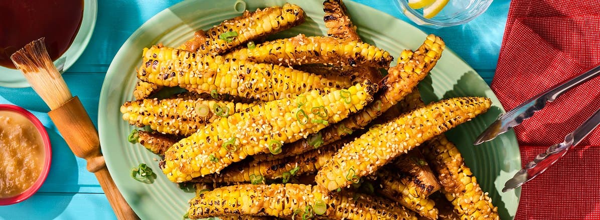 Overhead shot of platter of maple glazed and miso butter corn ribs topped with sliced green onions and sesame seeds