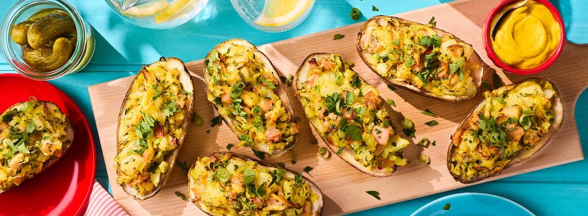 Baked potato skins on a wooden board stuffed with hot honey ham, cilantro, cheese, pickles,and parsley