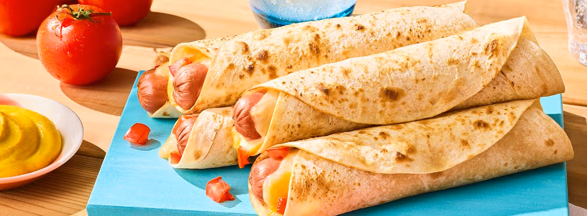 blue cutting board with five burrito hot dogs on a picnic table outside