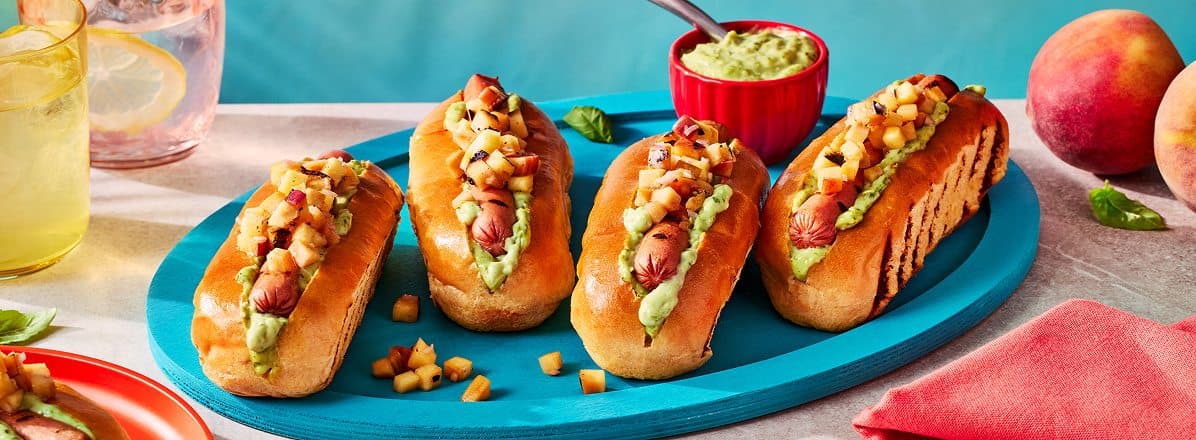 four grilled hot dogs layered with basil aioli and peach salsa on a blue platter