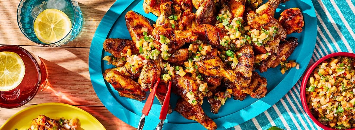 large blue platter of hot honey bbq sauce wings with peach salsa on top, and in a side dish