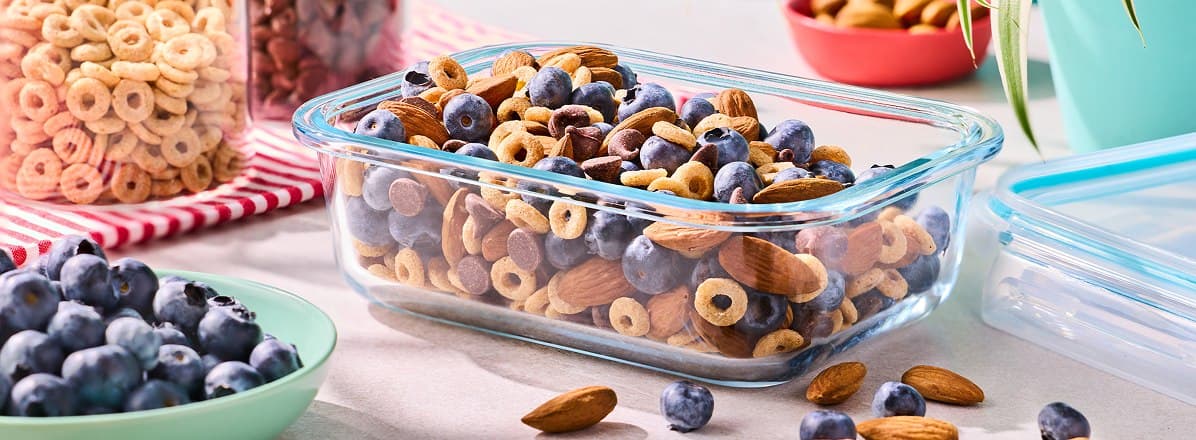 glass container of quick hiking trail mix - blueberries, almonds, dark chocolate chips, and cheerios - on a counter, ready to be packed for a hiking trip
