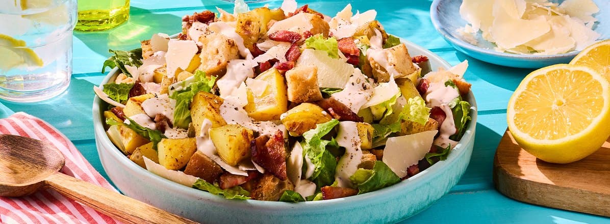 Caesar Potato Salad in a turquoise bowl topped with dressing with a side of fresh sliced lemons to the side