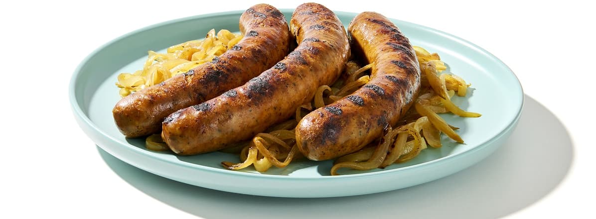 Three sausages and sauteed onions on a white plate