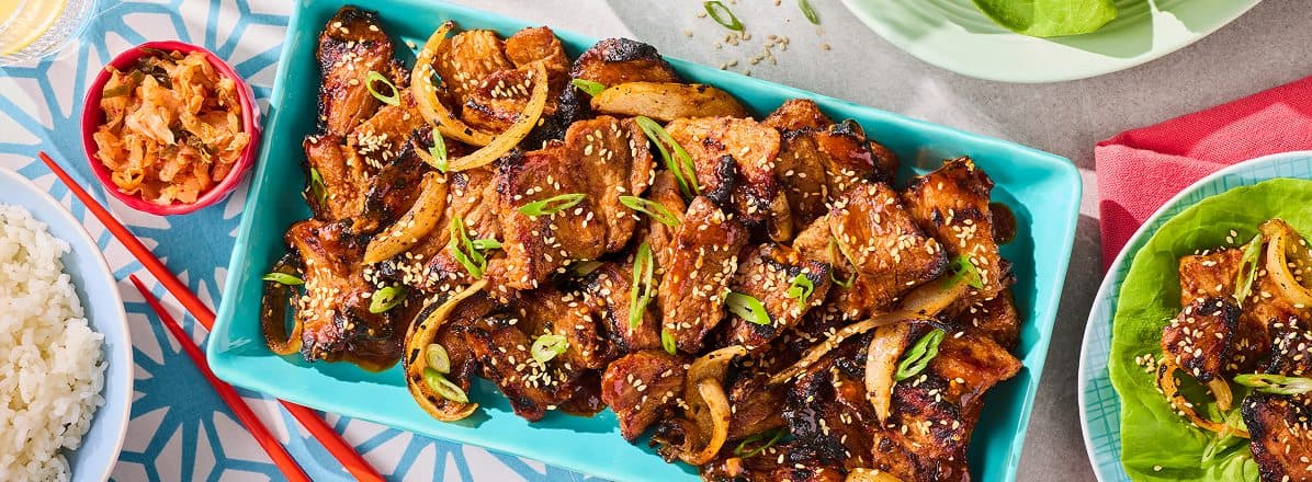 aqua blue rectangular serving platter with Korean-Style Spicy Grilled Pork Belly, side red chopsticks, butter lettuce and cooked white rice