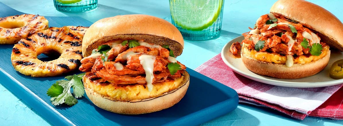 side view of two Al Pastor Whole Roasted Chicken Sandwiches with grilled pineapple to the side