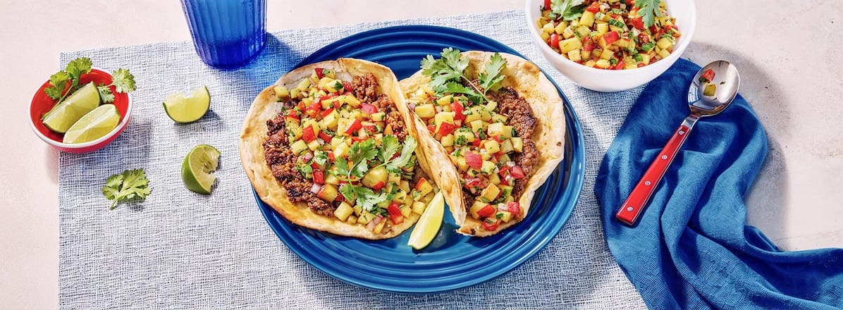 Two grilled smash burger tacos with peach salsa on blue dinner plate