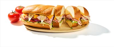 Dagwood sandwich filled with assorted deli meats, cheese, and veggies on a wooden cutting board. Half of the sandwich is cut into slices, showing the cross section.