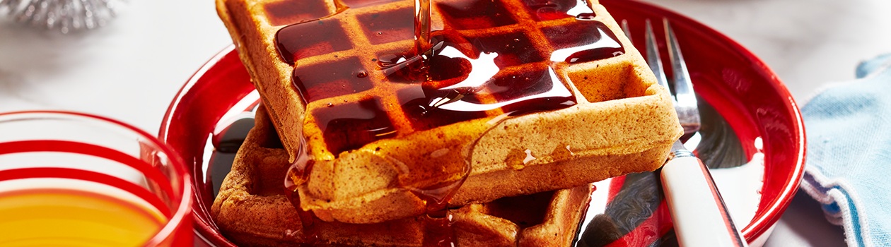 red plate with stack of waffles and maple syrup being poured overtop
