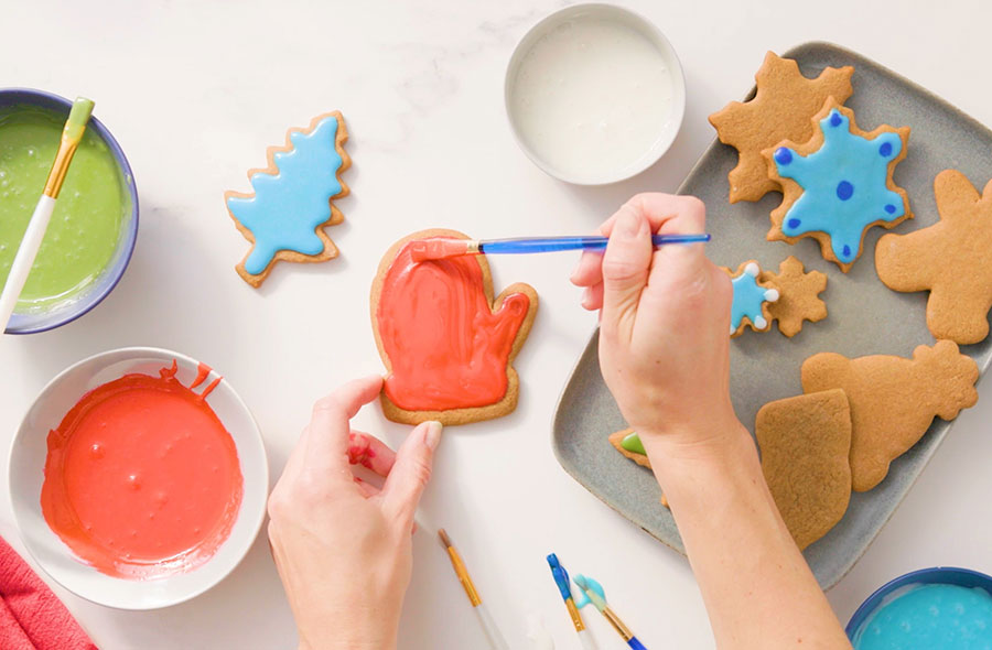 hands painting gingerbread cookies with a paintbrush and royal icing