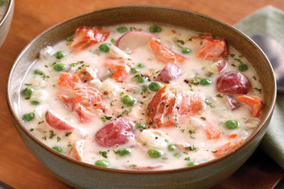 Seafood chowder in beige bowl on wooden board with spoon dipped into the Bowl.