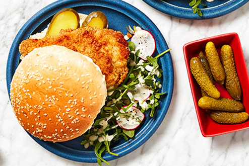 Two fried chicken sandwiches on blue plates with side of Pickles.