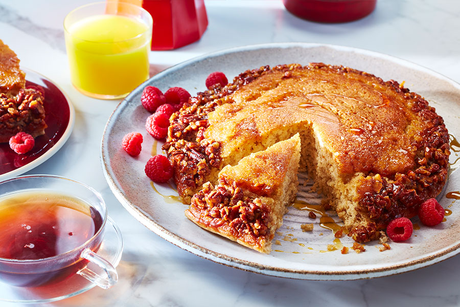 Family-size pancake with walnut-studded edges and fresh raspberry garnish on a white plate.