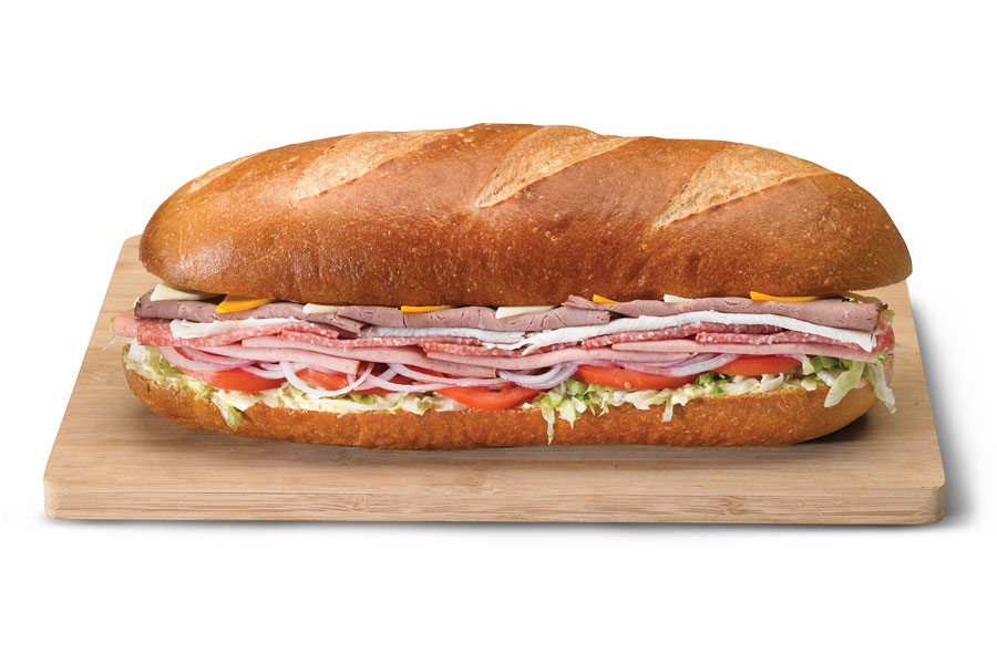 A deli department meat and cheese-stuffed dagwood sandwich served on a French loaf with shredded lettuce and tomato slices.