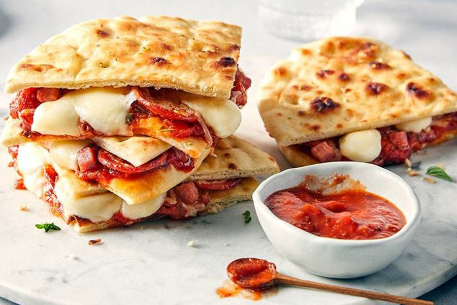 Grilled pizza sandwiches stacked up on around neutral marble serving board.