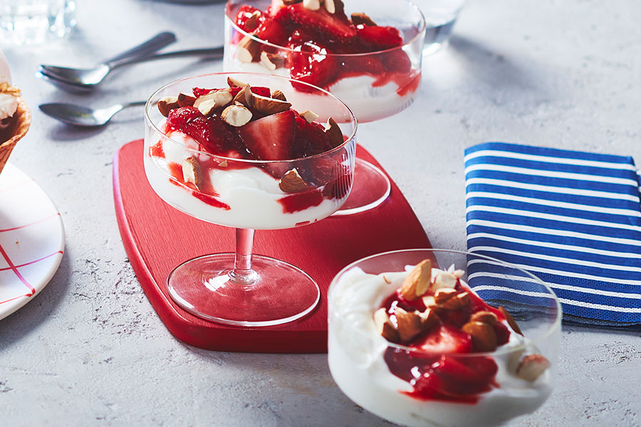 Ice cream sundae glass filled with creamy yogurt and red hot chili strawberries with almond slices