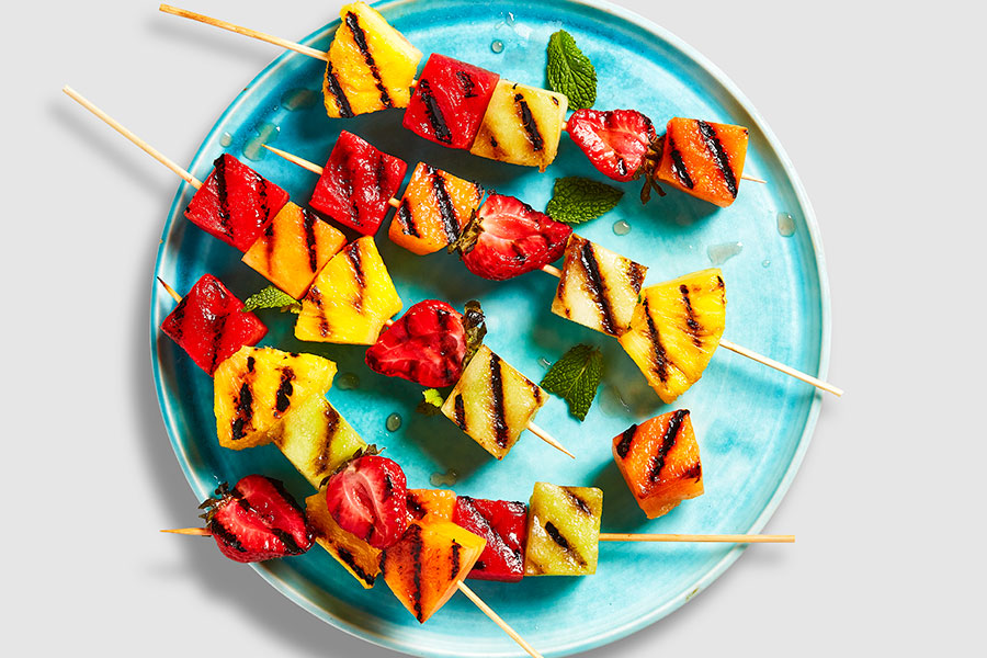 Grilled threaded skewers of strawberries, pineapple, watermelon, and cantaloupe on a blue plate.