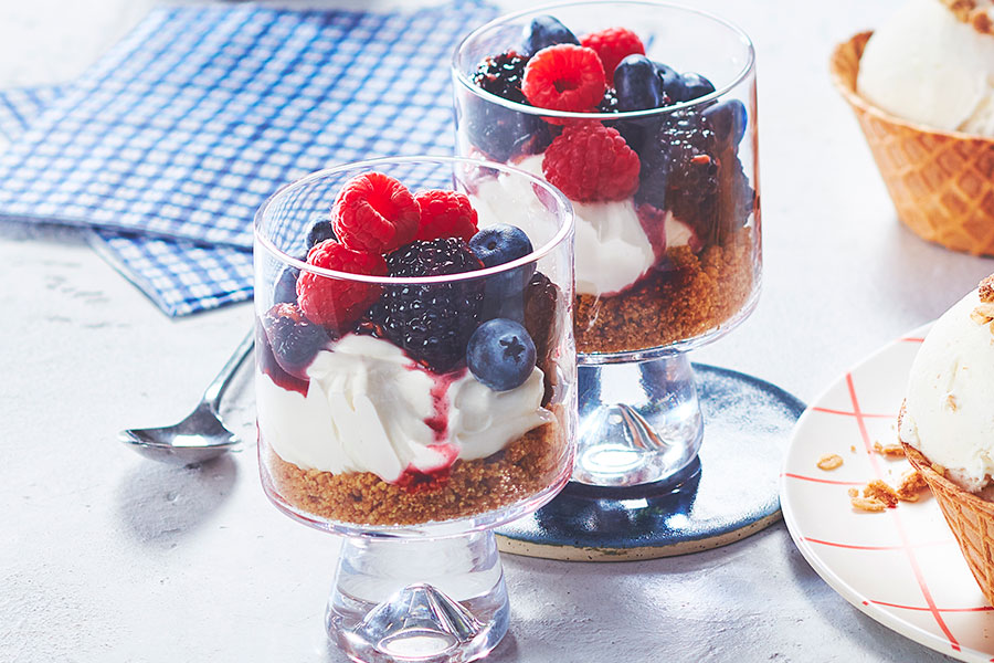 Fresh fruit dessert parfait in a glass cup on a table with a napkin and spoon to the side.