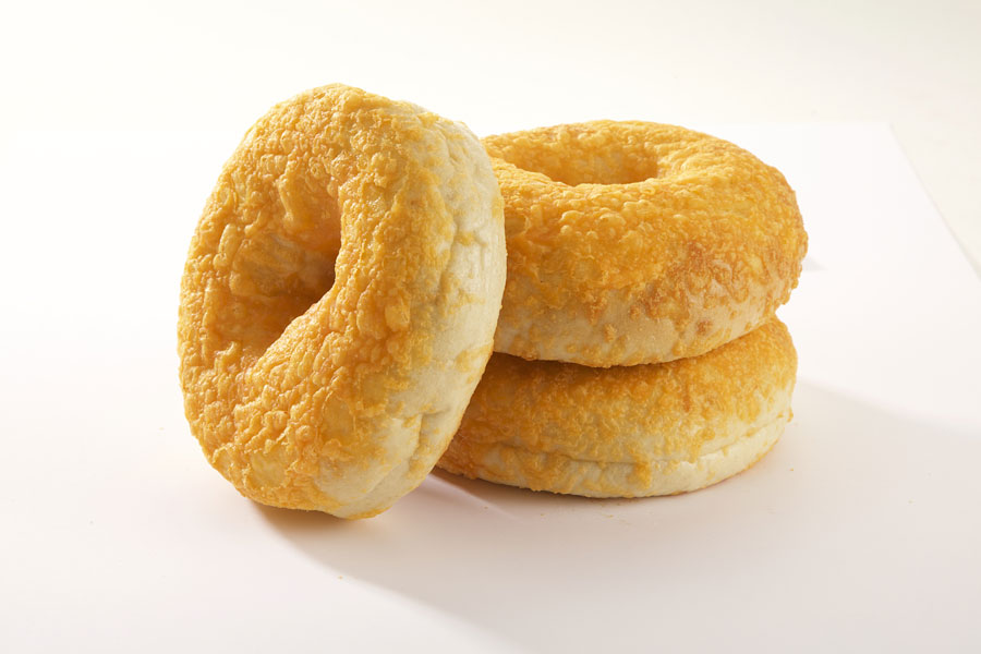 Three cheddar cheese bagels, two stacked on top of each other with one leaning against it on a white board.
