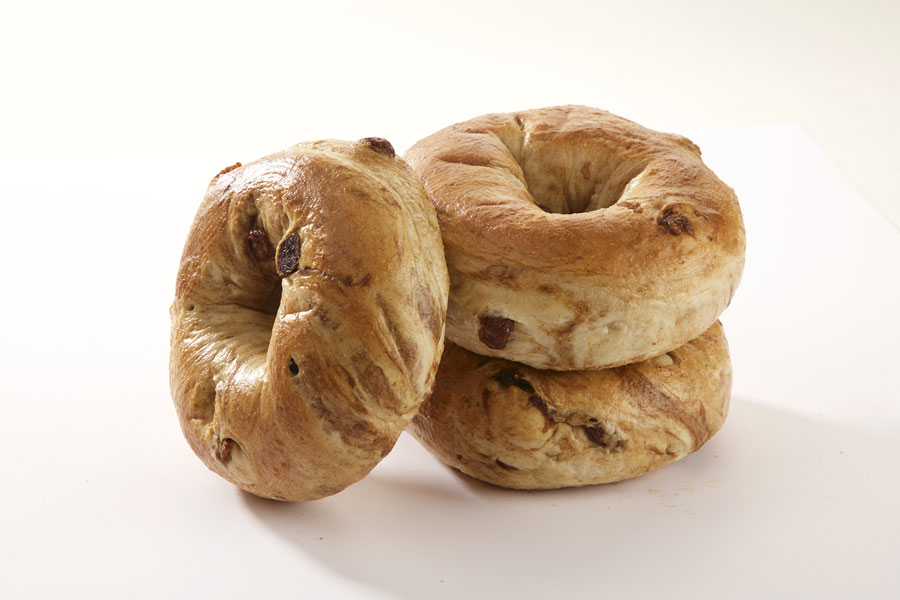 Three cinnamon raisin bagels, two stacked on top of each other with one leaning against it on a white board.