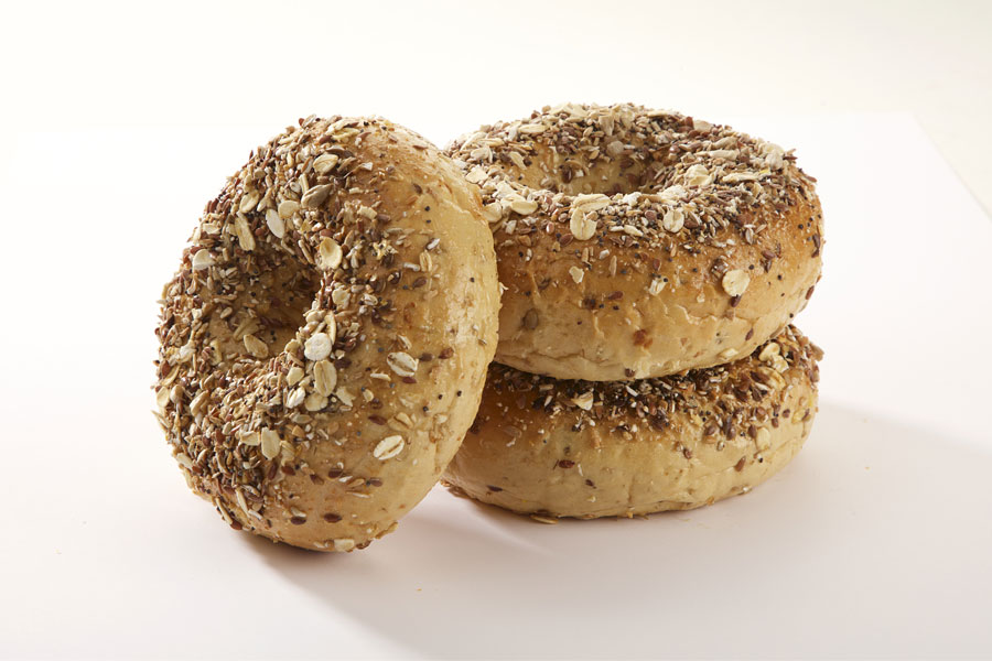 Three multigrain bagels, two stacked on top of each other with one leaning against it on a white board.