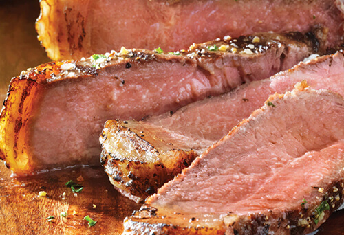 Sliced, spiced Sterling SilverÂ® Spiced Strip Loin Steak on a wooden cutting board.