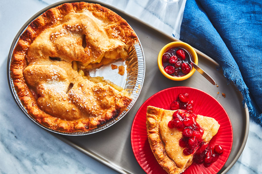 Apple pie with a slice taken out, with a side plate of apple pie topped with cranberry sauce and a side dish of cranberry sauce