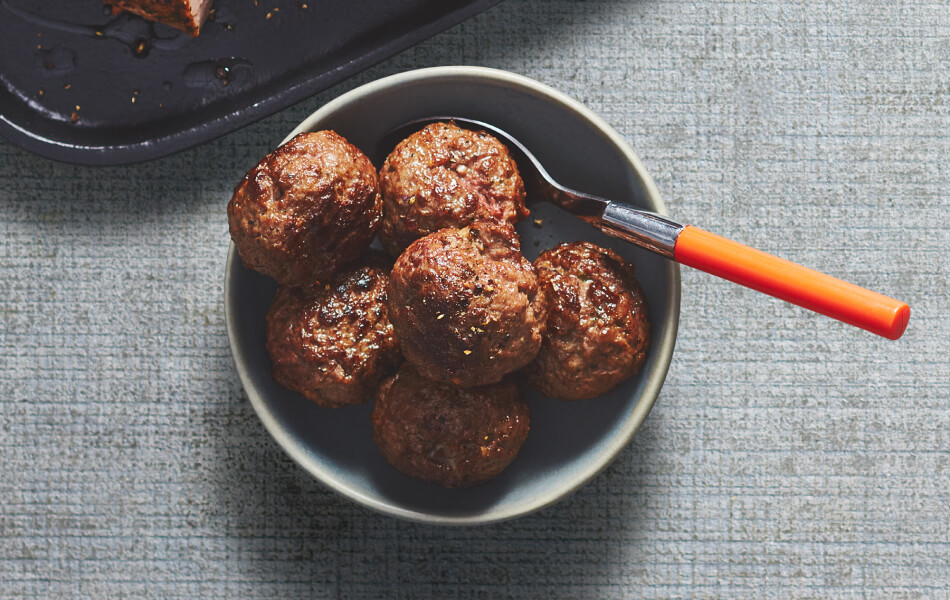 Meatballs in a grey bowl with a serving spoon in the bowl.