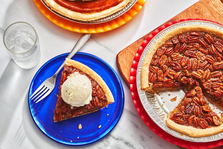 Pecan pie with a slice taken out, with a side plate of pecan pie, topped with whipped cream