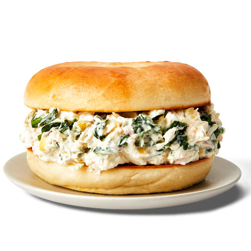 Plain bagel topped with cream cheese, sour cream, jarred artichoke, spinach, Mozzarella cheese and Parmesan on a white plate.