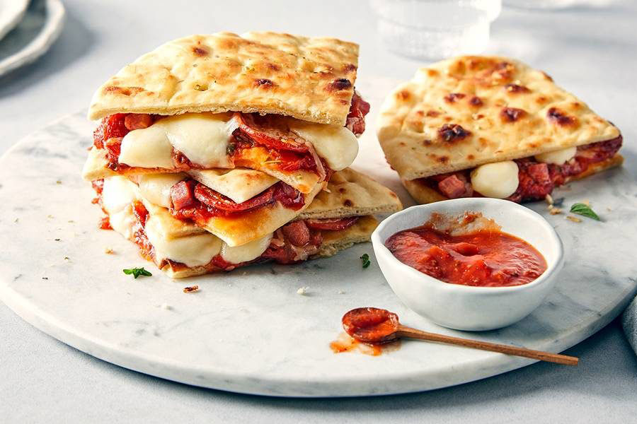 Grilled pizza sandwiches stacked around a neutral marble serving board.