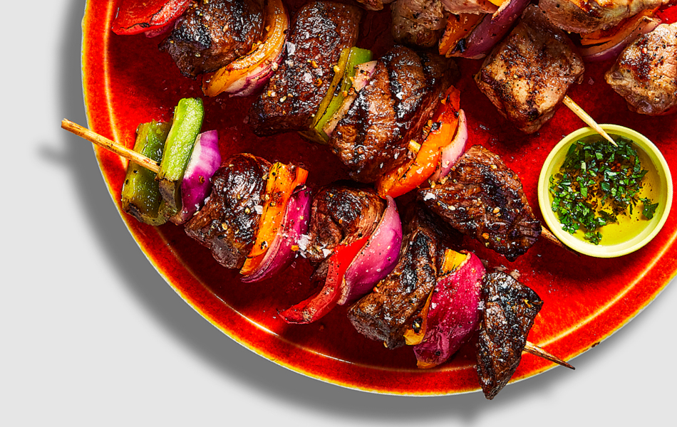 Beef kabobs threaded with red, yellow and green pepper slices on a grey plate.