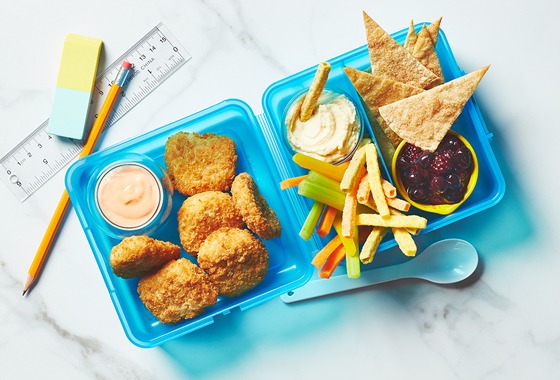 Kids blue bento lunchbox with chicken nuggets, dip, veggies, and dessert nachos.