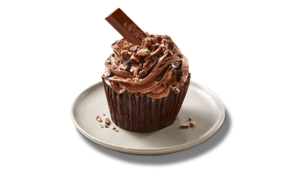 A single chocolate cupcake on a white plate frosted with chocolate icing and garnished with a piece of Kit Kat sticking out of it and candy bar crumbs.