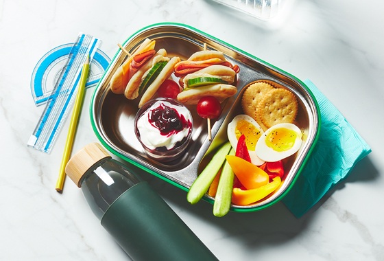 Kids bento lunchbox with ham and hummus, mixed snacks and a layered berry parfait.