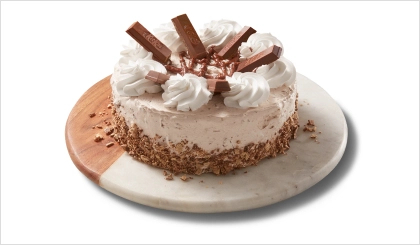 Chocolate triple layer cake covered in icing and KitKat crumbs on the side, topped with chocolate icing, and pieces of the candy bar.