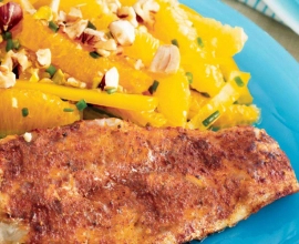 A piece of cod on a blue plate beside a salad of orange slices topped with nuts.