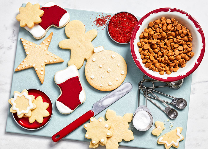 White marble countertop with a serving board of shortbread cookies partway through being decorated with icing and baking chips.