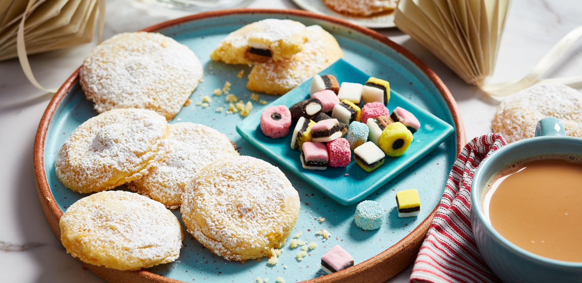 White marble tabletop with a blue plate of Allsorts-Candy-Stuffed Orange Shortbread Cookies and a short mug of tea off to the side