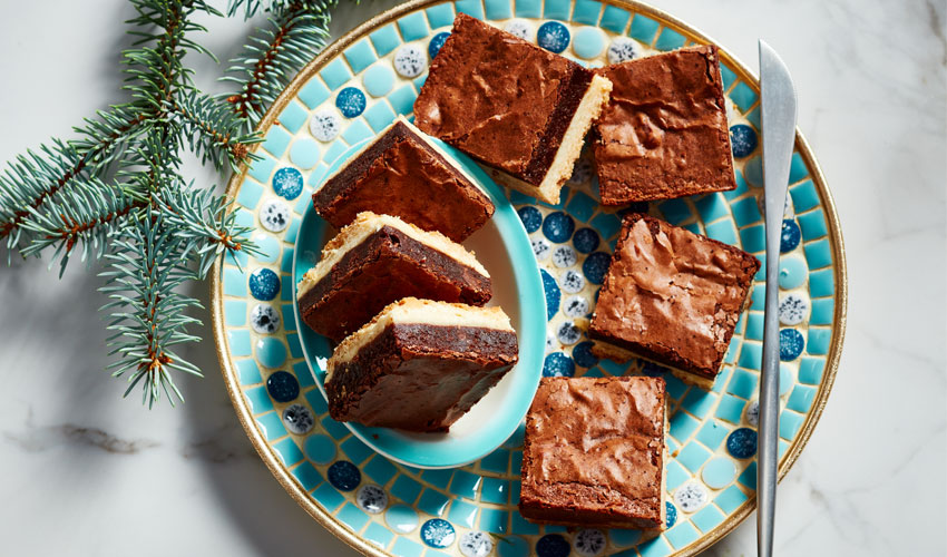 Blue and white tiled decorative serving plate with brownie shortbread bars, set on a white marble surface with holiday greenery off to the side.