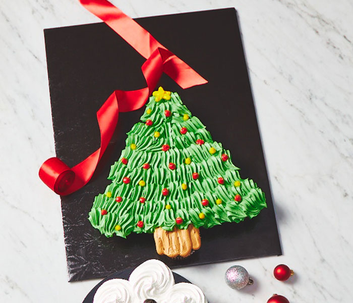 white marble surface with a black slate cutting board with a cupcake pull-apart cake decorated like a Christmas tree with green icing and icing lights.