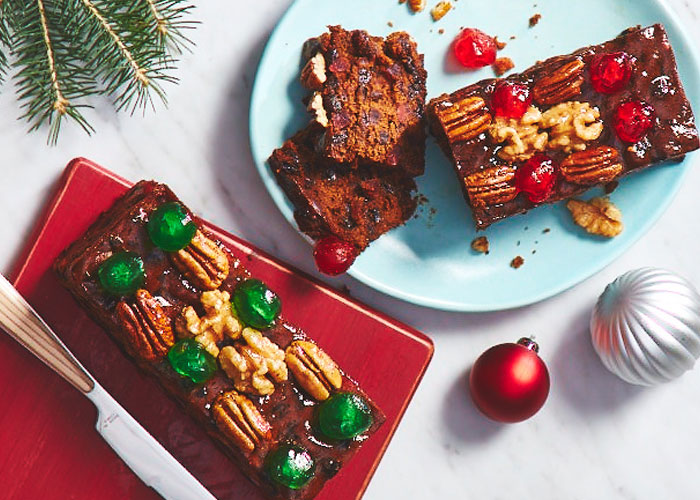 White marble surface with a light blue platter and red platter, both with a fruit cake, topped with glace cherries and nuts.