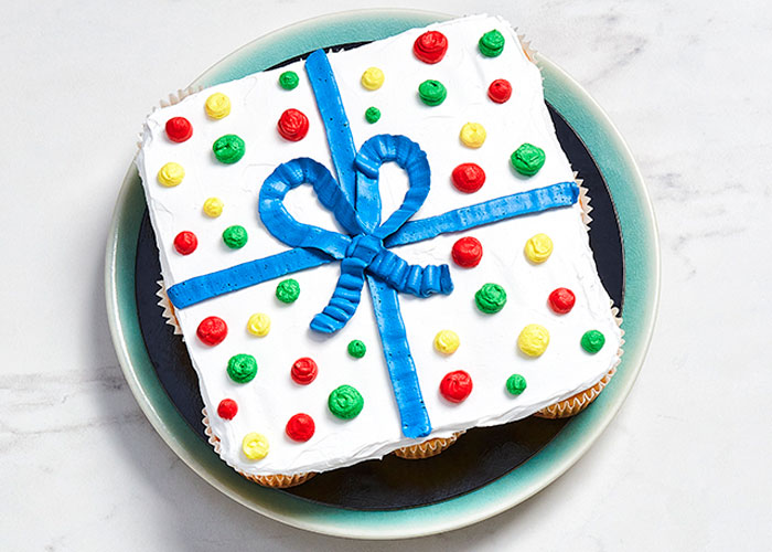 White marble surface with a light blue plate with a cupcake pull-apart cake with gift icing on top.