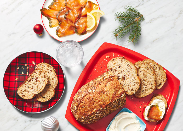 White marble surface with a red plate of wheat bread, sliced, and a dish of butter.