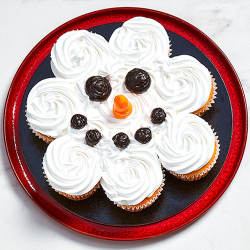 White marble surface with a red plate of cupcakes with a single snowman face designed into the icing of them all.