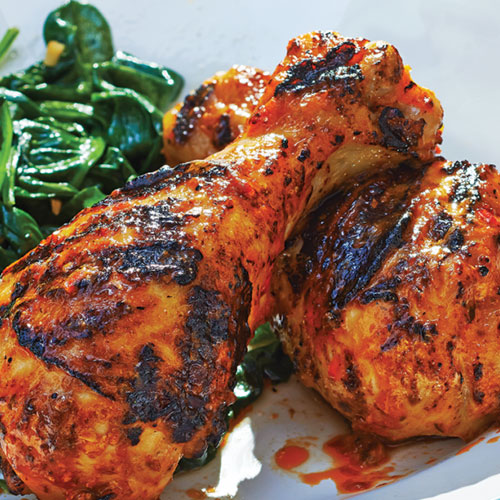Grilled chicken drumsticks with sauteed spinach on a white dinner plate
