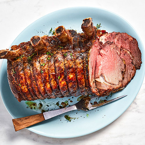 marble background with platter of cooked prime rib roast beef, with a carving knife