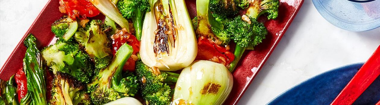 Red serving platter with charred bok choy and broccoli.